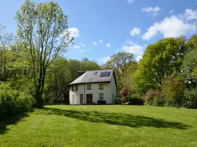a white house on a green field with trees at Henllys Lodge in Cilycwm