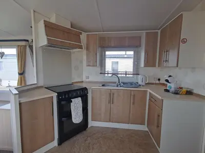 a kitchen with wooden cabinets and a black stove top oven at Snowdonia Holiday Sea Beach and Mountains view in Llwyngwril