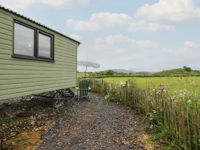 a green house with a chair next to a fence at Shepherd's Hut at Penrallt Goch in Blaenau-Ffestiniog