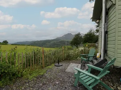 a patio with two green chairs and a fence at Shepherd's Hut at Penrallt Goch in Blaenau-Ffestiniog