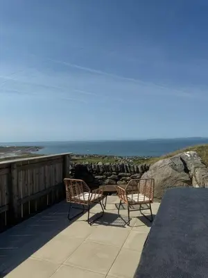 two chairs and a table on a balcony overlooking the ocean at Bay View shepherds hut with hot tub in Llanfair