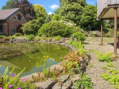 a garden with a pond in front of a house at The Mytton at Mill Barn in Craven Arms