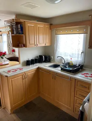 a kitchen with wooden cabinets and a sink and a window at Lovley 3 bedroom Static Caravan in Clarach Bay in Aberystwyth