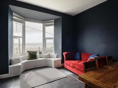 a living room with a red chair and a window at Tonnau Yr Oleu or Waves of Light in Barmouth