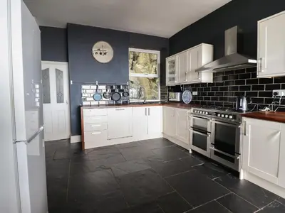 a kitchen with white cabinets and a black wall at Tonnau Yr Oleu or Waves of Light in Barmouth