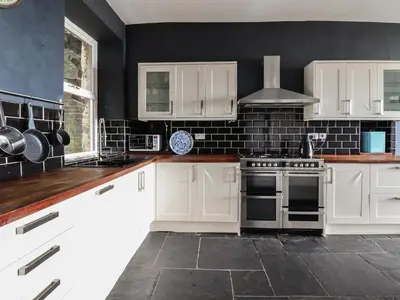 a kitchen with white cabinets and a black wall at Tonnau Yr Oleu or Waves of Light in Barmouth