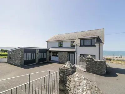 a large white house with a fence and the ocean at Melin Y Plas in Barmouth