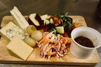 a plate of food with cheese and vegetables on a cutting board at The Boughton Peterchurch - Pub Grub & Bed in Peterchurch