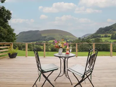 a table and chairs on a deck with mountains in the background at Caban Tirion in Machynlleth
