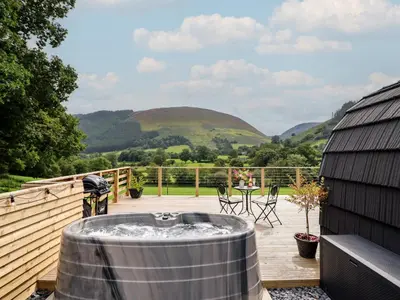 a hot tub on a deck with mountains in the background at Caban Tirion in Machynlleth
