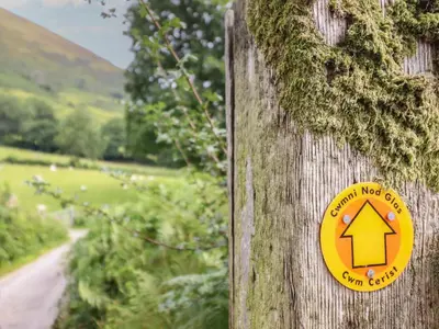 a yellow sign on a wooden post with a path at Caban Tirion in Machynlleth