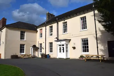 a large white building with two benches in front of it at River Wye Hostel in Hereford