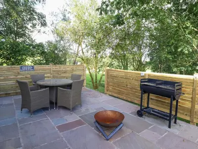 a patio with a grill and a table and a piano at Orchard Lodge in Corwen