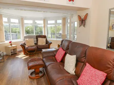 a living room with a leather couch and a butterfly on the wall at Trem-Yr-Afon in Lampeter