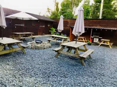 a group of picnic tables with umbrellas and a fire pit at Bunkhouse Accommodation in the Heart of Snowdonia in Dolgellau
