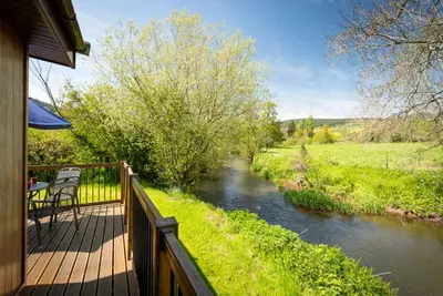 a deck with a table and chairs next to a river at Ash Lodge in Craven Arms
