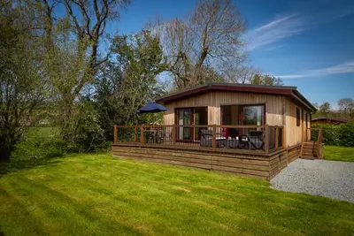 a small cabin with a deck on a grass field at Ash Lodge in Craven Arms