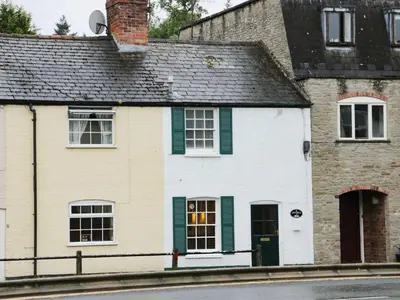 a white house with green shutters on a street at Troutbeck Cottage in Ludlow