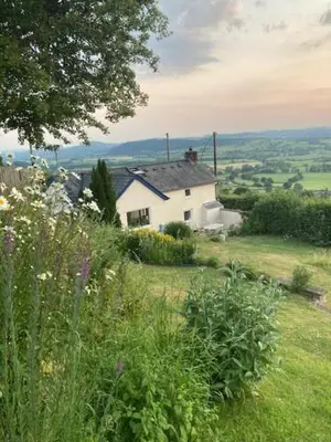 a white house on top of a grassy hill at Trinity Cottage in Welshpool