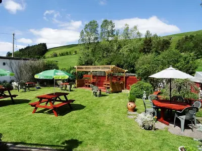 a garden with picnic tables and umbrellas on the grass at Llew Coch B&B formerly The Red Lion inn in Llanfihangel-nant-Melan