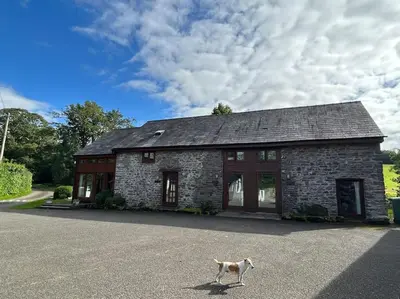 a dog walking in front of a stone house at Happy Horse Cottages in Sennybridge