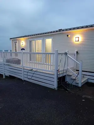 a mobile home with a white fence and lights at Newquay Haven caravan 42x14 with Ocean Views in New Quay
