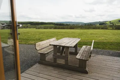 a wooden bench sitting on a deck with a field at Hafren by Wigwam Holidays in Llanbrynmair