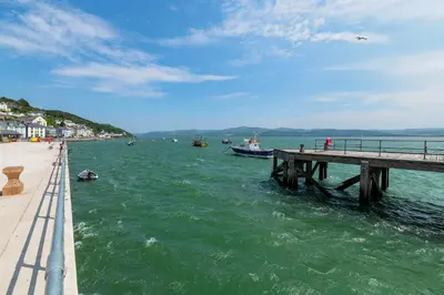 a pier with boats in the water next to a beach at 2 Bed Ground Floor Beach Location in Aberdyfi