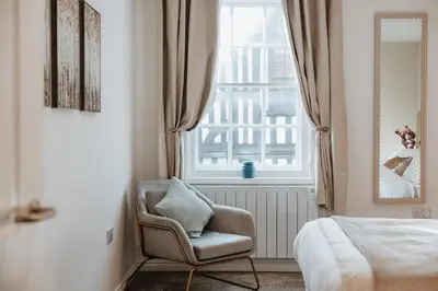 a bedroom with a chair in front of a window at 2 Bed Apartment Overlooking the Square Step Out to Shops & Dining in Shrewsbury