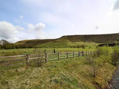 a fence in a field with a hill in the background at Ty Hir at Blaenbrynich Farm in Brecon