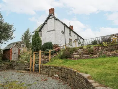 a white house on a hill with a stone wall at Rowan Cottage in Bishops Castle