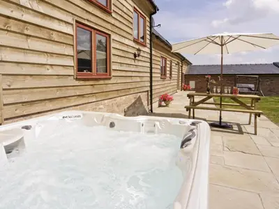 a hot tub outside of a house with an umbrella at Cefnaire Isaf in Newtown