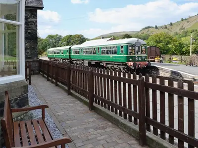 a green train on the tracks next to a bench at Porter's Lodge in Glyn-Dyfrdwy