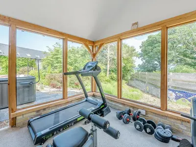a gym with a treadmill and dumbbells in a room with windows at West Barn in Llansadwrn