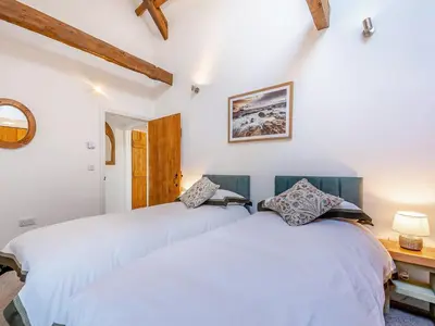 two beds in a bedroom with white walls at West Barn in Llansadwrn