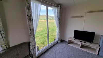 a living room with a tv and a large window at Lyons Sunnysands Caravan Park in Barmouth