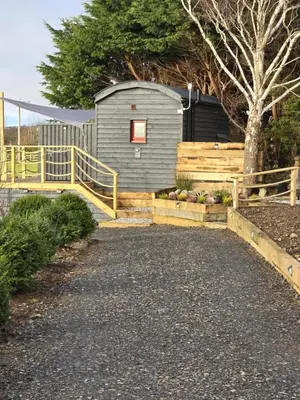 a small shed with a wooden fence and a walkway at Ty'r Bugail - Shepherds Hut in Llanddwywe