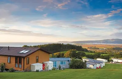 a house on a hill with a green yard at 3 Bed Caravan - Sleeps 6 - Pets - Parking - Wifi in Borth