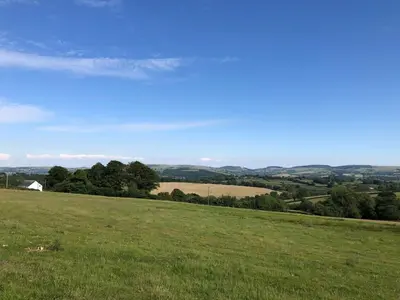 a field of green grass with a house in the distance at Secluded farmhouse with views in Cwrt-newydd