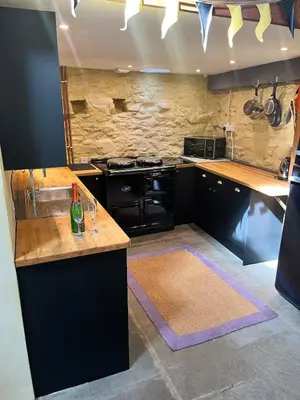 a kitchen with black appliances and a stone wall at Glovers cottage private hot tub and super king in Llanrhystyd