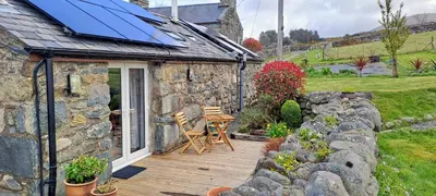 a stone cottage with a wooden deck with a table and chairs at Bryn Teg Barn in Dyffryn