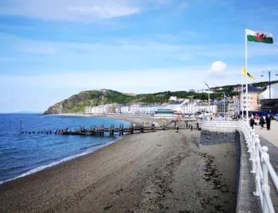 a beach with a flag and people walking on it at Gold Standard Luxury and Modern Static Caravan at Clarach Bay in Aberystwyth