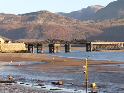 a bridge over the water with mountains in the background at Sandcastles in Barmouth