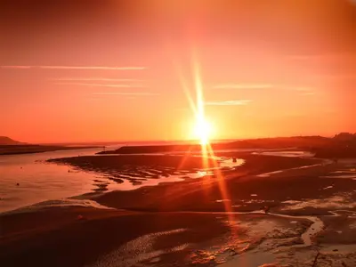 a sunset over a beach with the sun setting at Sandcastles in Barmouth