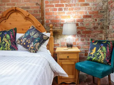 a bedroom with a bed and a chair next to a brick wall at The Courtyard Cottage in Llangollen