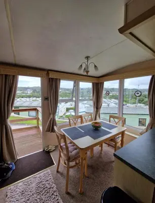 a dining room with a table and chairs and windows at 2 Bed Caravan - Sleeps 6 - Pets - Pool - Parking in Aberystwyth