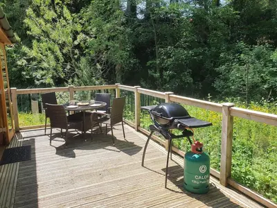 a grill on a deck with a table and chairs at Swn Y Nant Lodge with hot tub Brecon in Brecon
