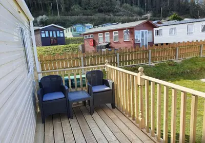 two chairs sitting on a deck with houses in the background at Pet Friendly 3 Bed Static Caravan in Clarach Bay Spacious and Cozy Stay in Aberystwyth