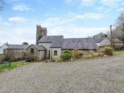 an old stone house with a church in the background at Y Cartws in Llanybydder