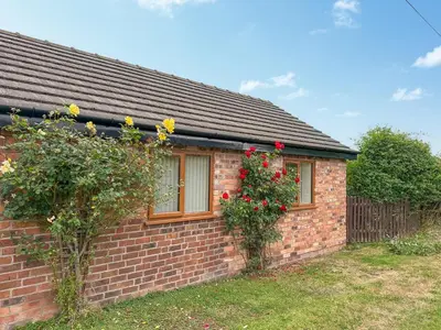 a brick house with two windows and roses at The Old Milking Parlour in Melverley